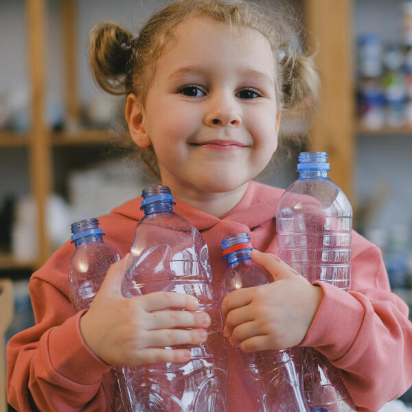 banner image Little girl smiling and holding 4 single use plastic bottles
